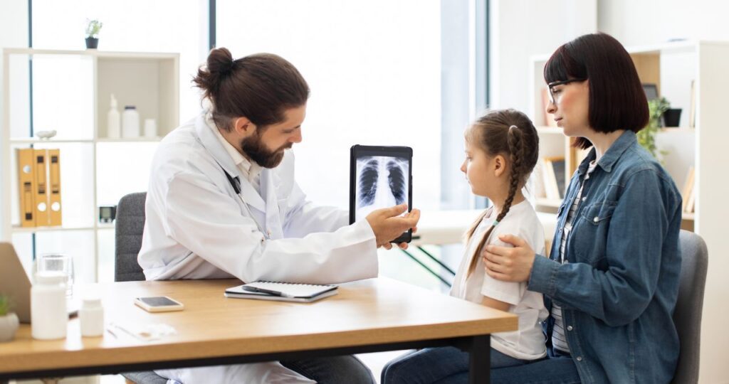 A doctor shows chest X-ray images on a tablet to a young girl and her mother during a medical consultation in an office. Urgent Care Omaha